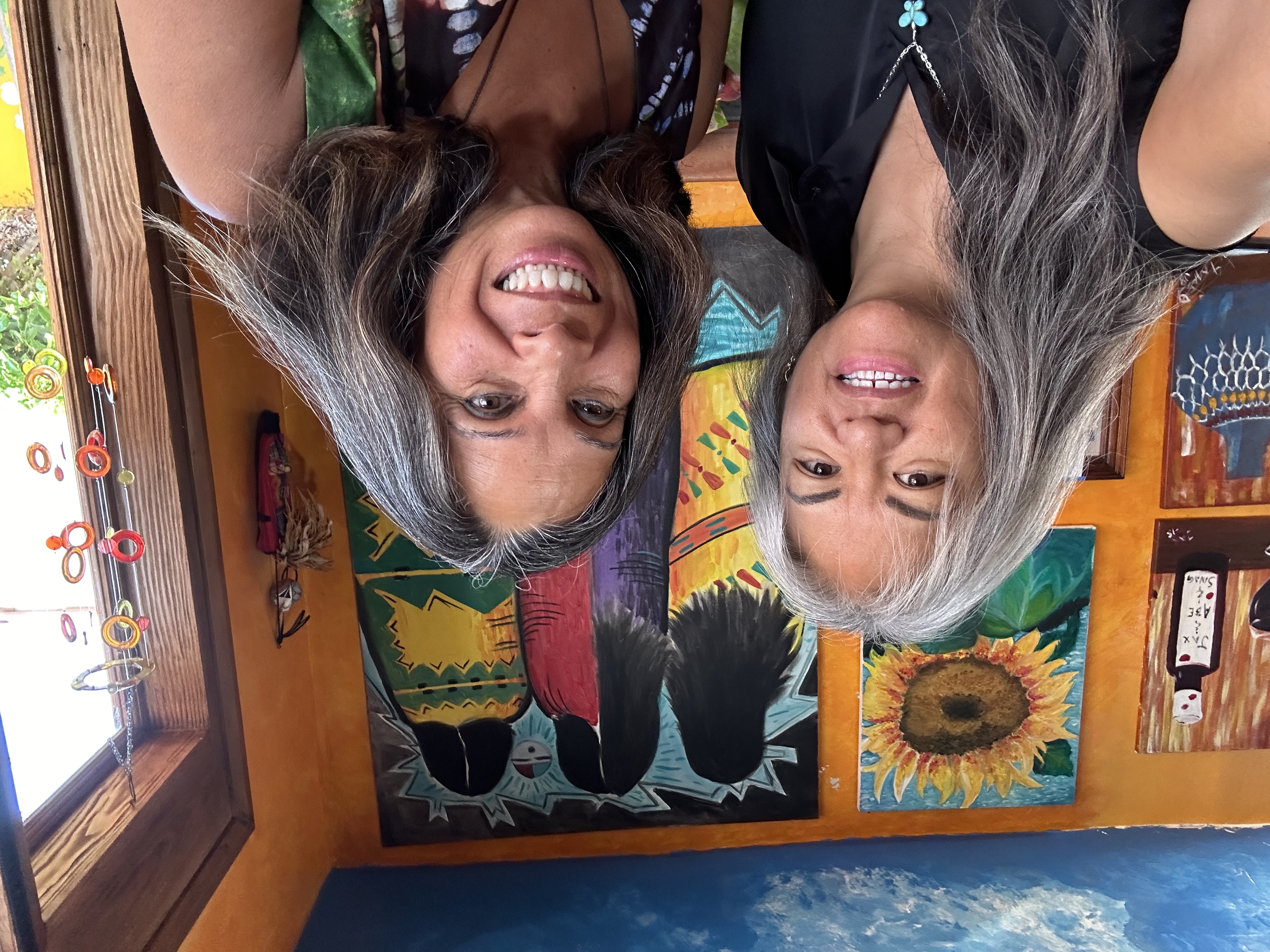 Paula Julian and Jacqueline "Jax" Agtuca smiling, standing in front of a vibrant mural featuring cat and sunflower illustrations.