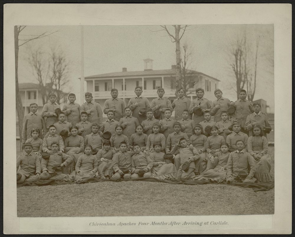 Group photo of Chiricahua Apache students four months after arriving at Carlisle, posed in multiple rows outdoors.