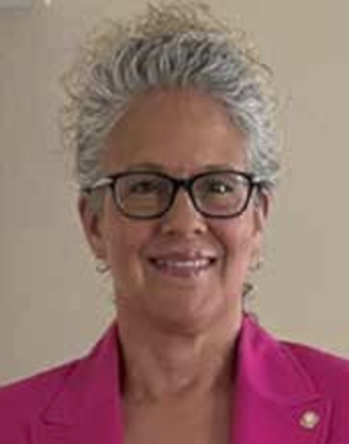 Portrait of Sherriann Moore smiling, wearing glasses and a pink blazer.